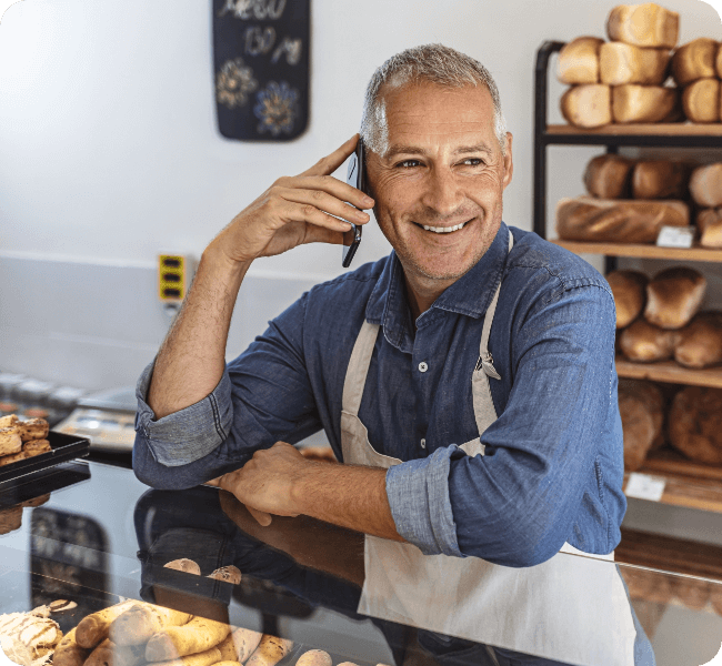 Gray hair man in blue shirt and apron placing a call from bakery