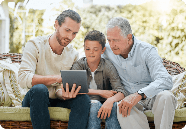 Grandpa, father, and son viewing tablet while sitting on couch